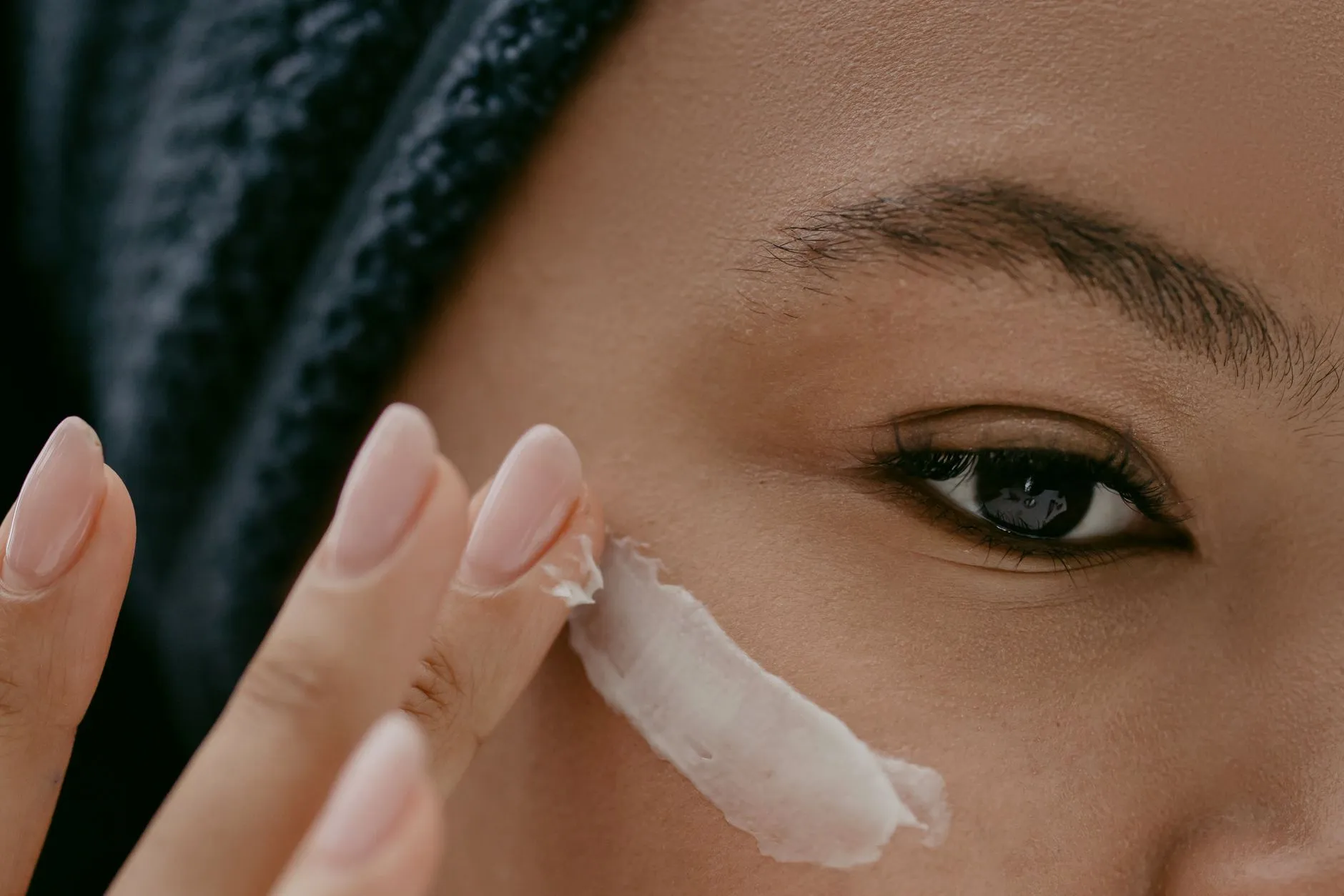 Mulher espalhando creme na maçã do rosto, em close
