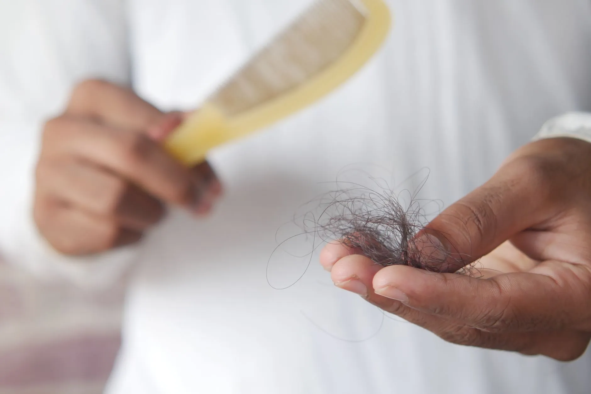 Mão segurando um tufo de fios de cabelo caídos ao lado de um pente