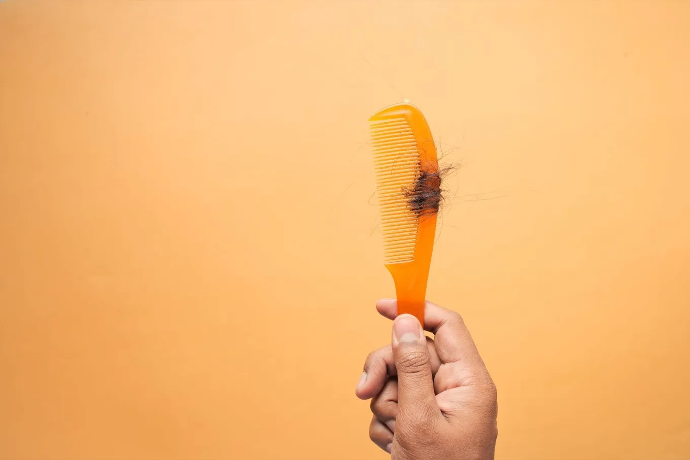 Mão segurando um pente laranja com um chumaço de fios de cabelo caídos preso nos dentes